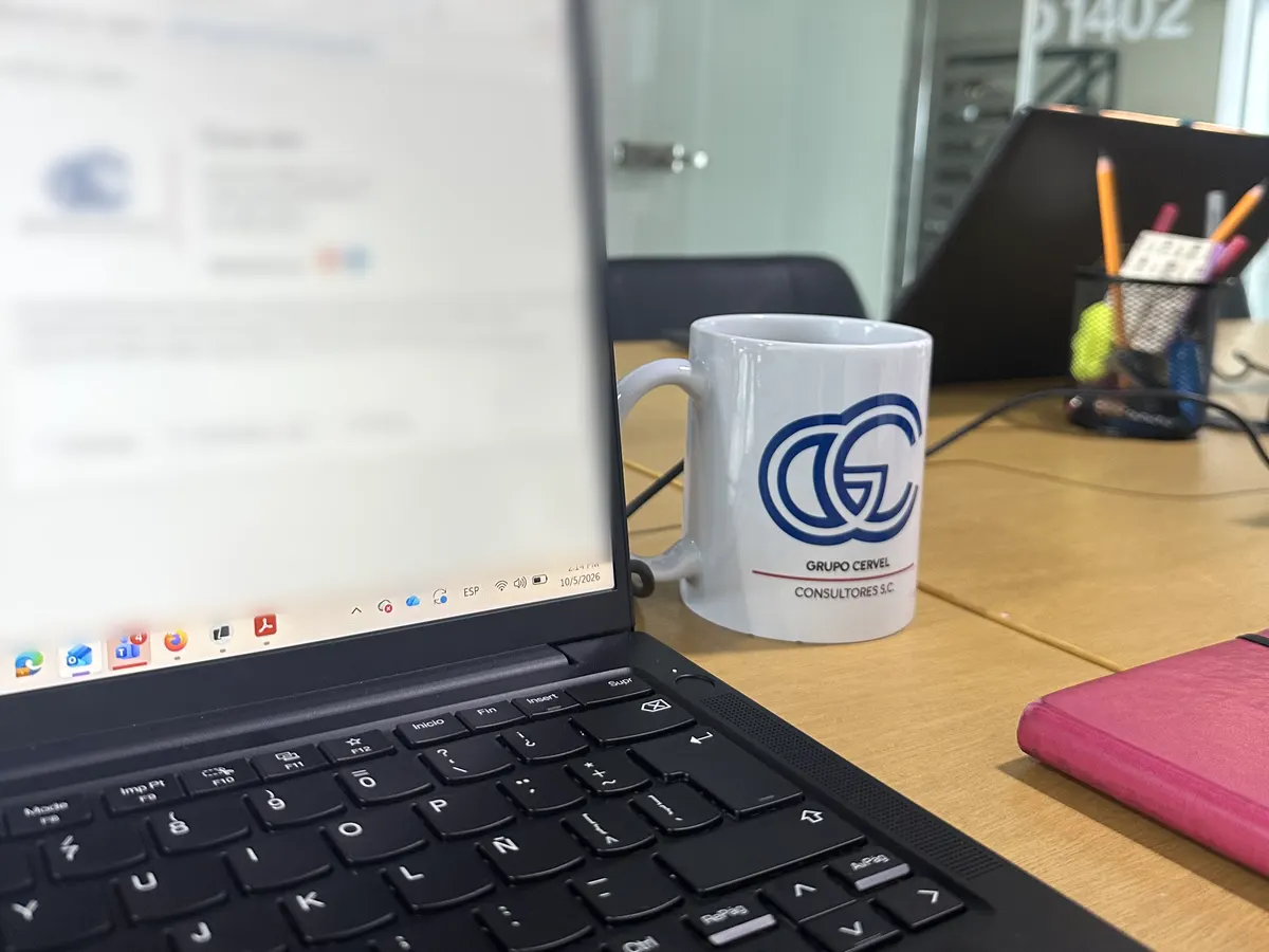 Laptop y taza con el logotipo de Grupo CerVel en una mesa de trabajo del despacho