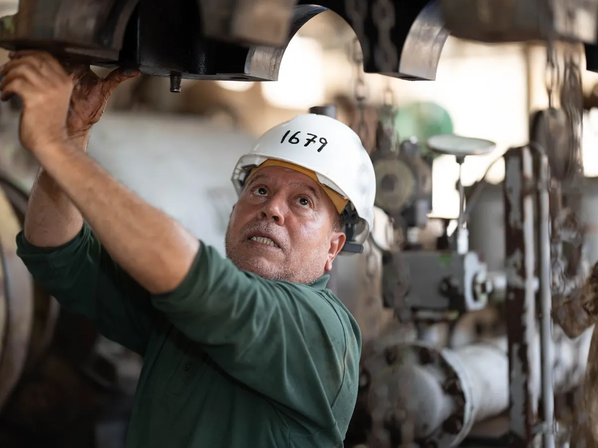 Técnico con casco blanco trabaja en el mantenimiento de maquinaria en una planta industrial